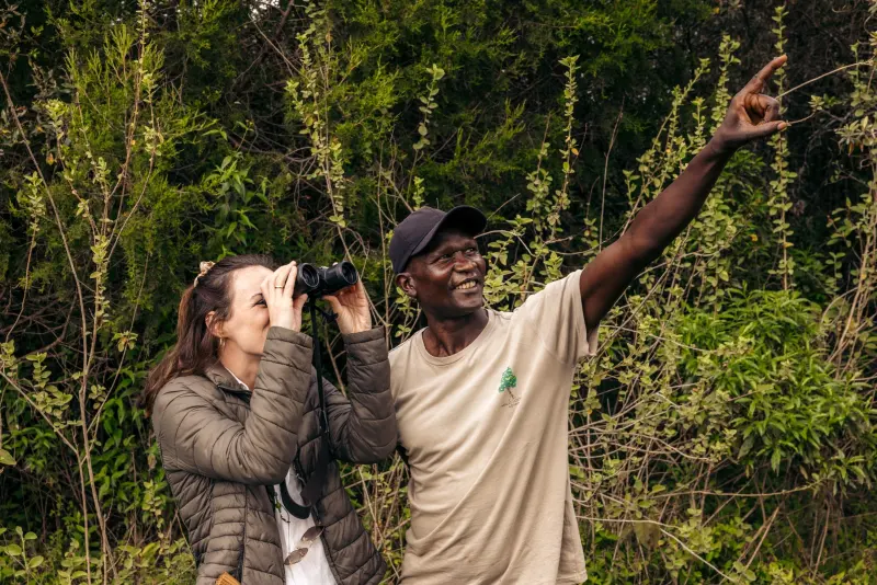A Malu guide pointing out a bird to a guest with binoculars