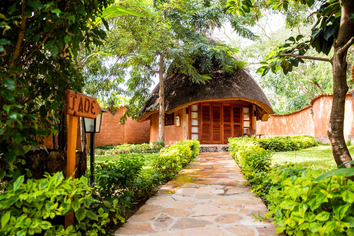 A flagstone path lined with shrubs leading to the Jade bungalow’s thatched entrance, its carved name sign in front