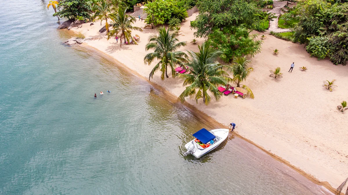 The private sand beach from above, with loungers under the palms, a moored boat and swimmers in the clear water