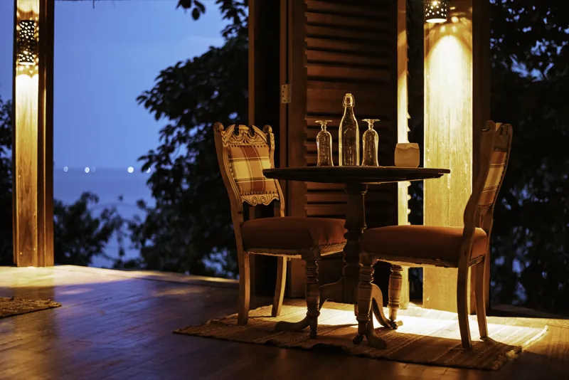 A lamplit terrace table set with glasses, looking out over Lake Tanganyika at dusk