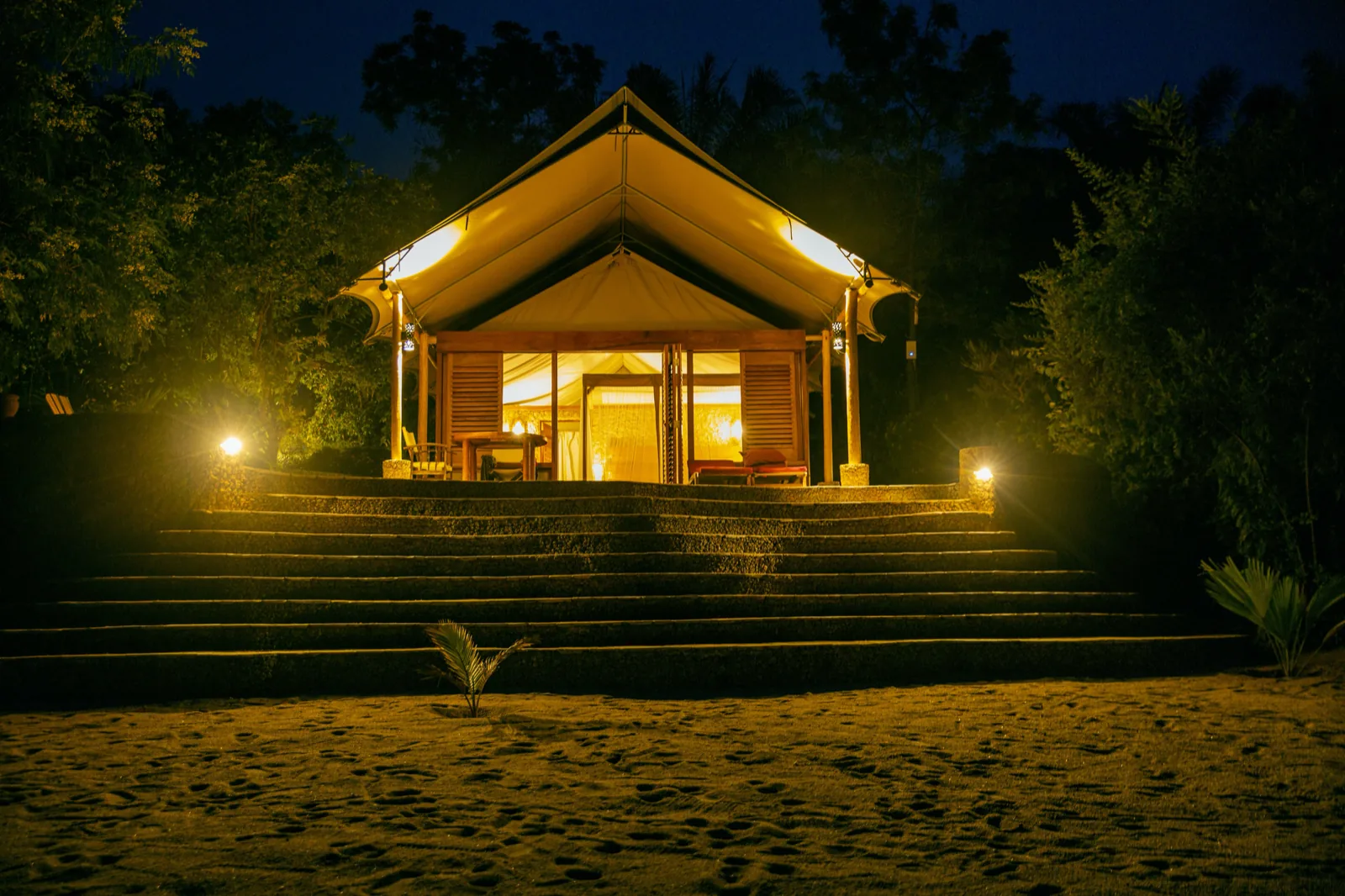 The tent glowing warmly above the beach steps under a deep blue night sky