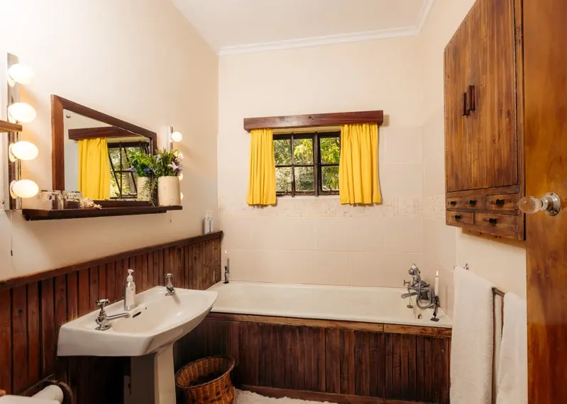 The bathroom with a timber-panelled bath and yellow curtains at the window