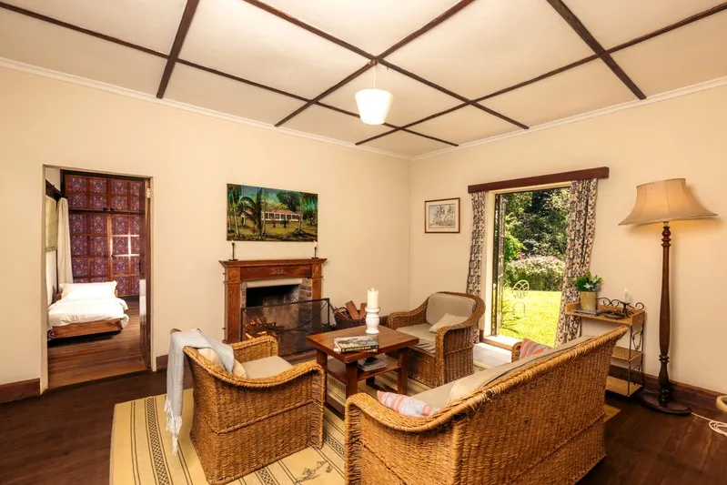 The cottage sitting room with wicker armchairs around the fireplace, the bedroom beyond