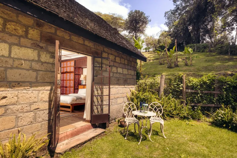The stone Mahindu Cottage with its door open to the bedroom, a white table and chairs on the grass outside