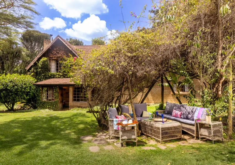 Mahindu House behind its garden, sofas and a low table set out on the lawn under the trees