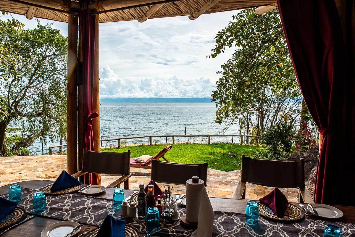 A laid dining table under the bamboo pavilion, looking out across the lawn to the lake