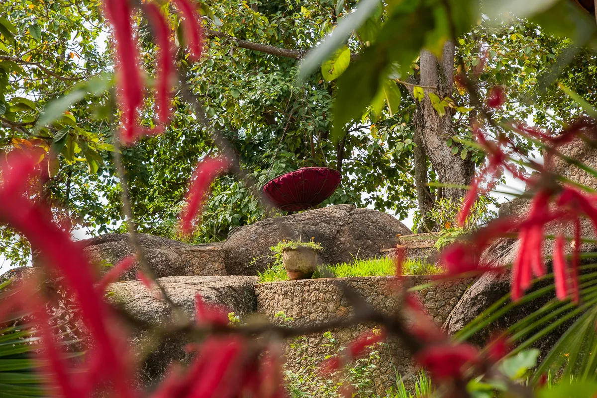 A parasol resting on granite boulders framed by red chenille flowers in the villa garden