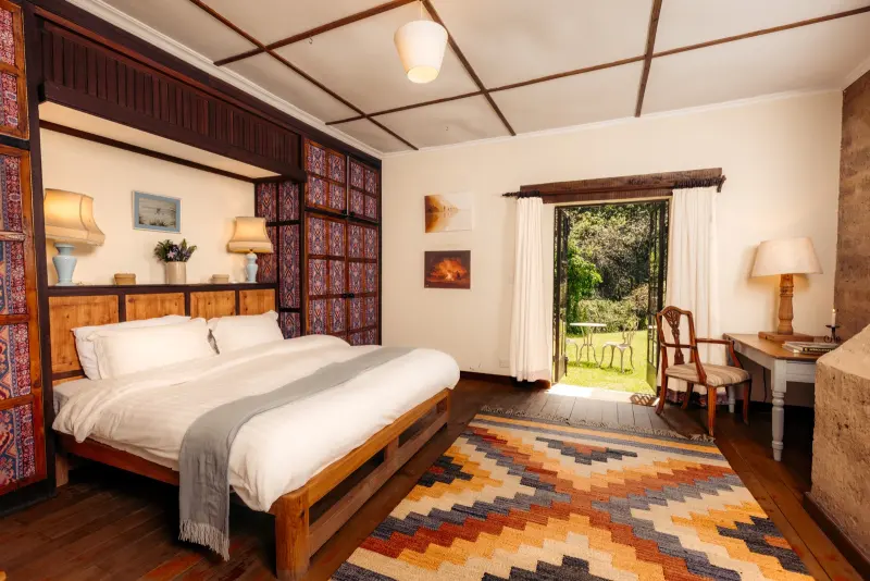 A double bedroom with a kilim rug, bedside lamps and a door open to the garden