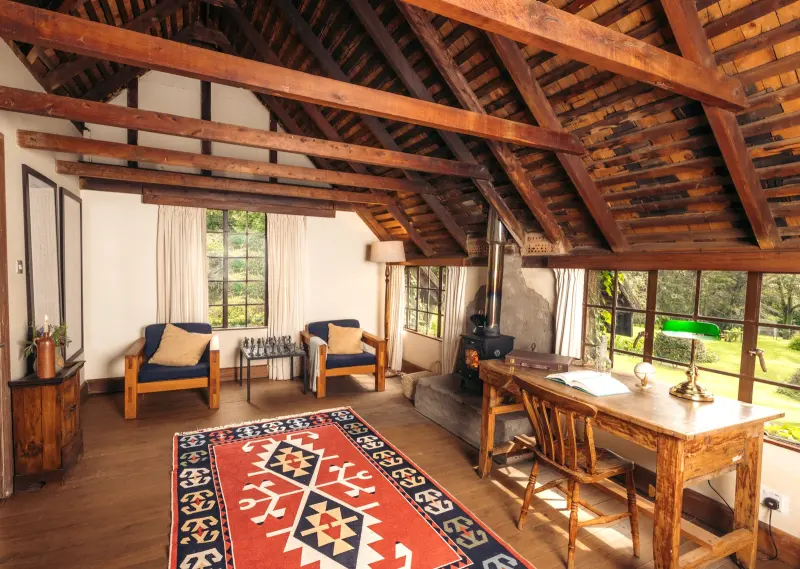 A timber-beamed lounge with armchairs, a writing desk and a red kilim