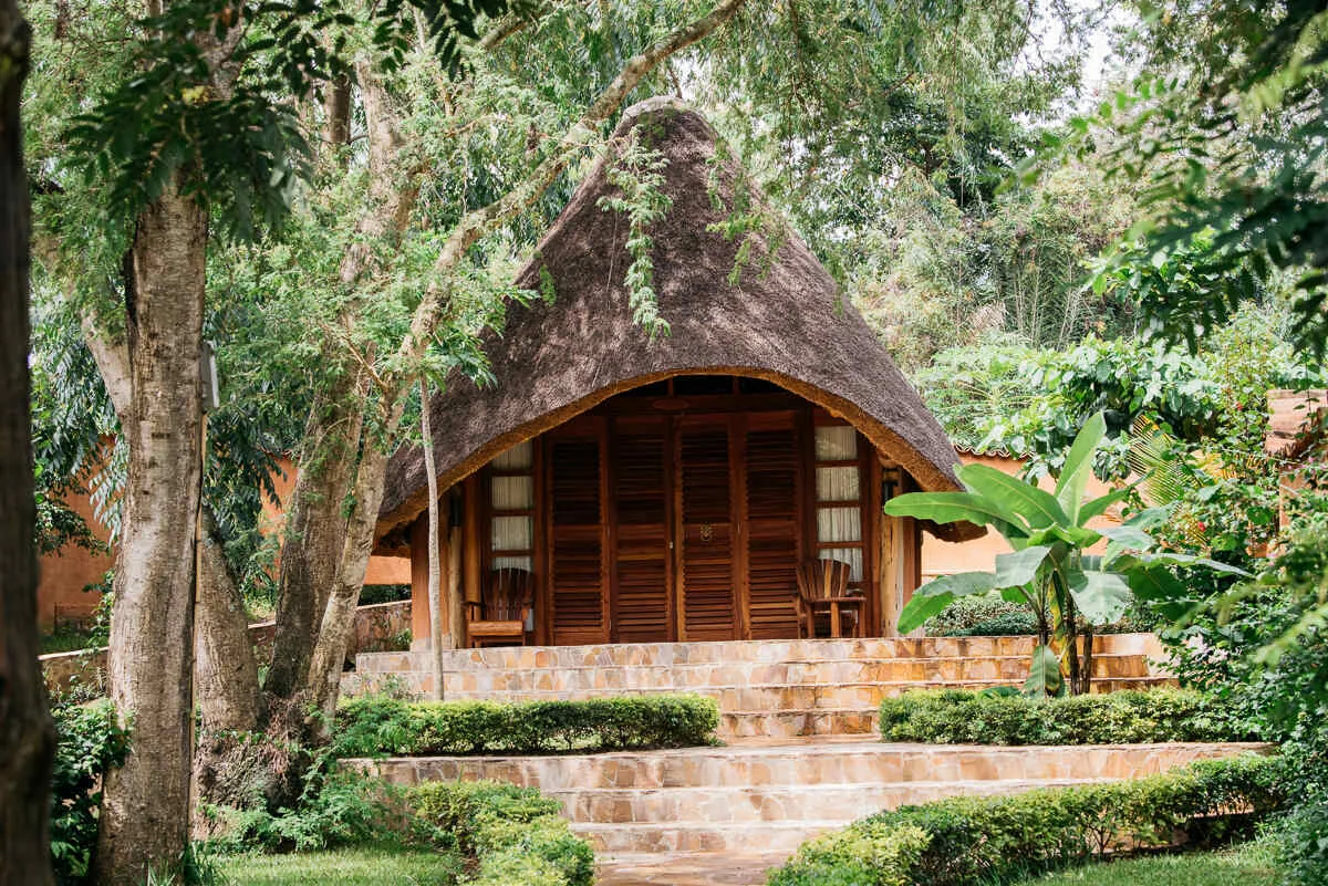 A thatched bungalow with wooden louvred doors and a veranda, reached by broad stone steps through clipped hedges