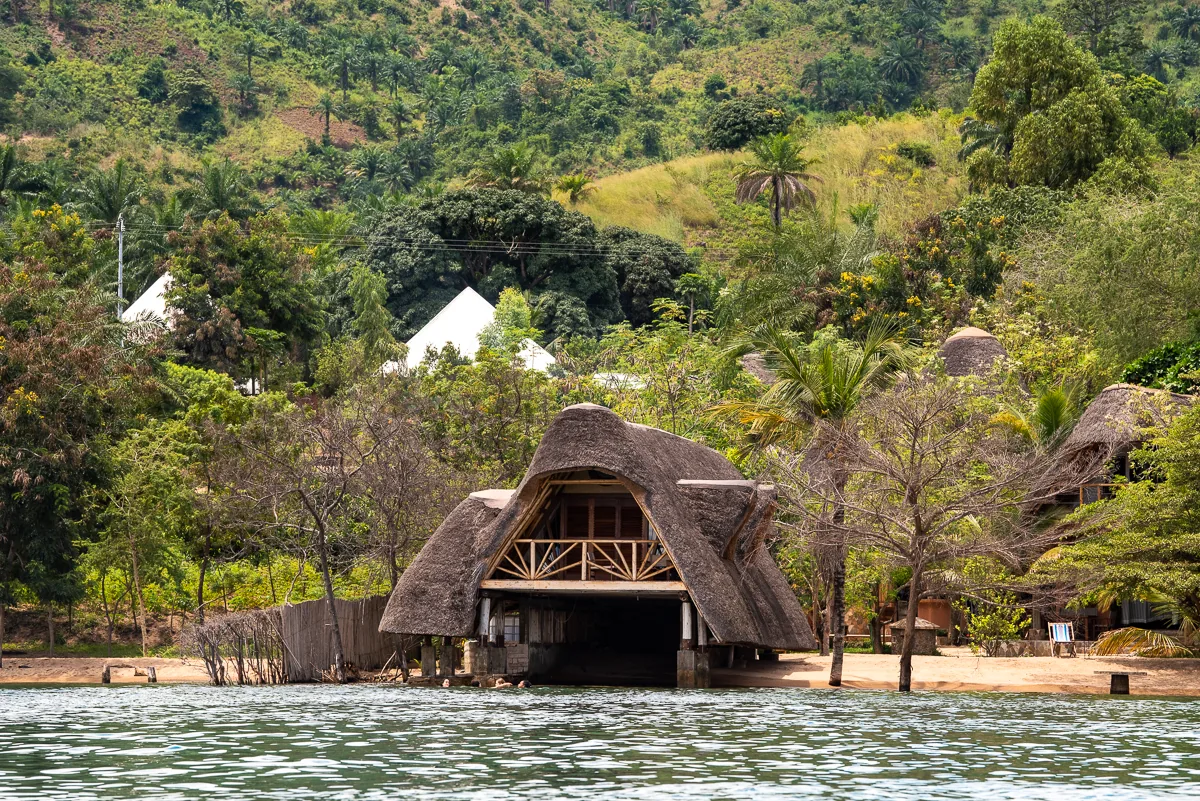 The wooded shoreline of Sunstone Beach seen from the water, thatched roofs and tents among the trees
