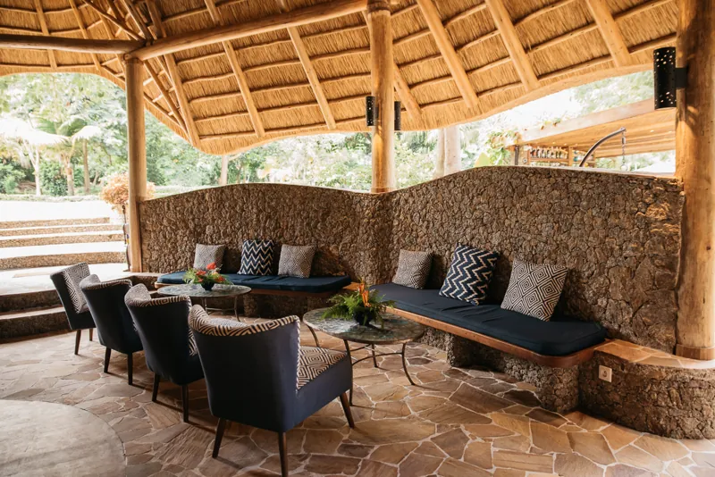 An open-sided thatched lounge with navy cushioned benches, armchairs and stone-topped tables