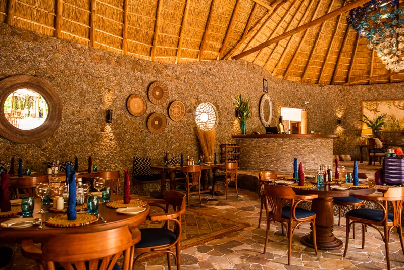 The round thatched dining room with stone walls, set tables and a bar counter