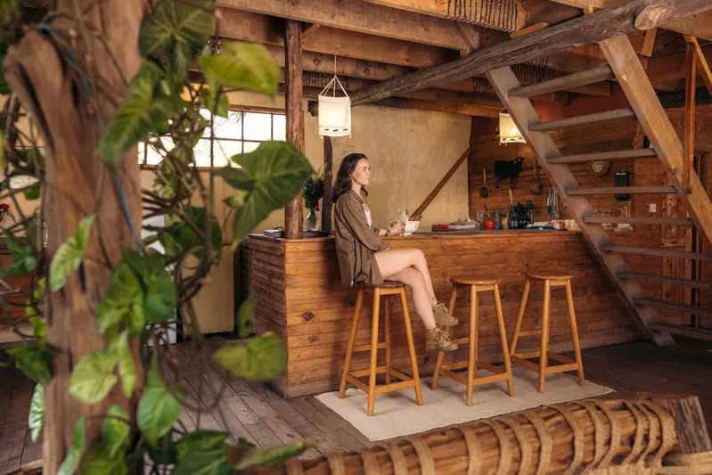 A guest at the Treehouse bar counter, timber stools and the stair to the upper floor behind