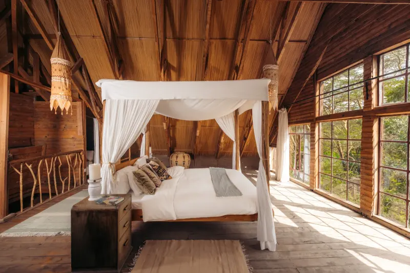 A four-poster bed under the sloping timber roof, windows on every side